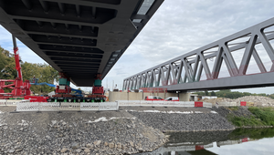 Das Foto zeigt, dass die Brücke bereits am anderen Ufer von einem weiteren SPMT in Emfpang genommen wurde.